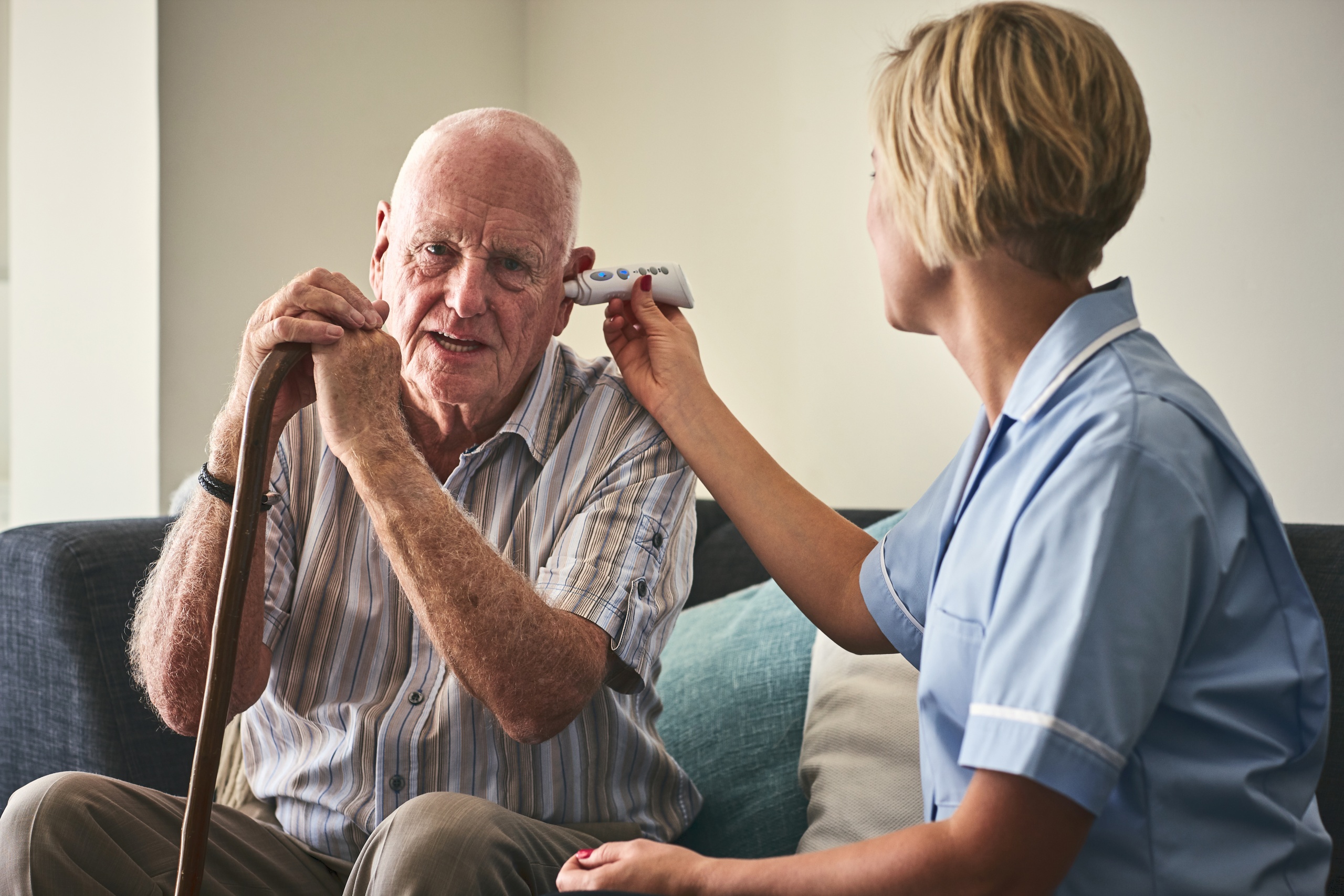 Female nurse checking patient temperature while sitting on sofa at care home