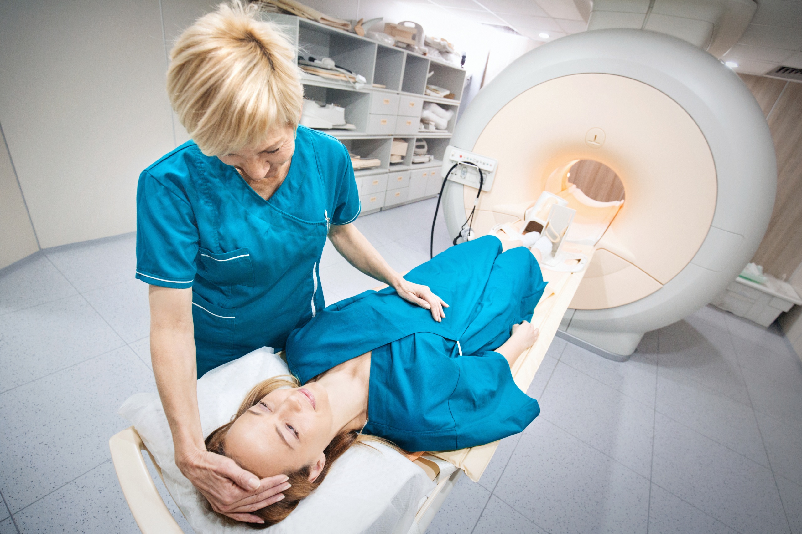 Closeup top view of a technician preparing an early 40's female patient for an MRI scan of a foot. The technician is explaining the procedure to the patient and that there's nothing to be afraid of.
